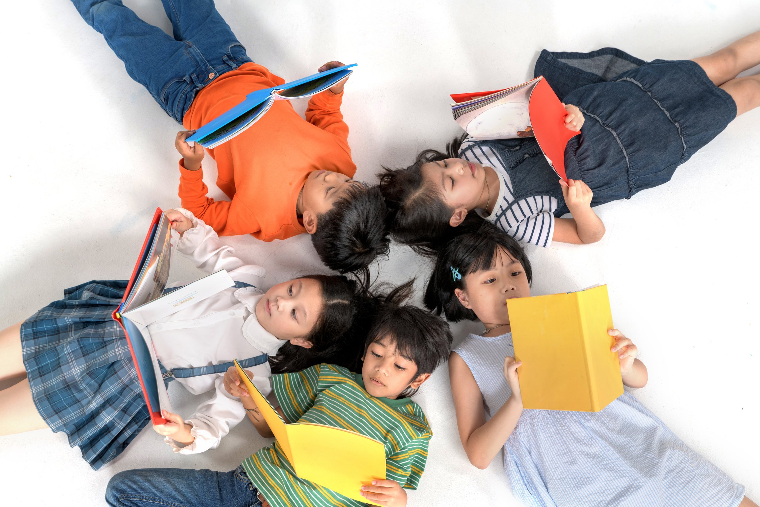 Kids reading book laying on the white floor ,head to head, in a circle group, preschool library,Kindergarten school education concept